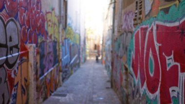 Grafiti kaplı dar sokakların bulanık görüntüsü, kenar mahalle kültürünün tipik dağılmış arka planlarını vurgulayarak canlı renklerle kentsel sokak sanatı sahnesini akla getiriyor..