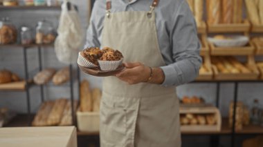 Ekmek ve fırınlanmış mallarla dolu bir fırında elinde muffin tutan İspanyol bir adam, içinde taze hamur işleriyle dolu samimi bir dükkan sergiliyor..