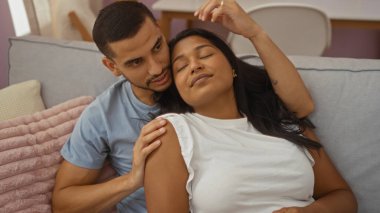 Kadın ve erkek rahat bir oturma odasında kanepede birlikte rahatlıyor, İspanyol bir evde sevgi ve aile sergiliyorlar..