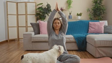 Güzel sarışın bir kadın yoga minderinde otururken evinde evcil köpeğiyle yoga yapıyor..