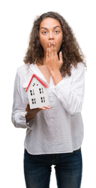 Şaşkın bakışlı genç siyahi kadın şeffaf arka planda ev modelini tutuyor.