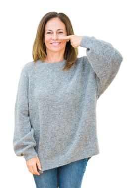 Kış süveteri giyen olgun bir kadın şeffaf arka planda burnunu işaret ediyor.