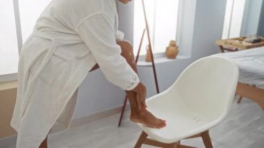 Bir kadın spa odasında bacağına losyon sürüyor. Yumuşak ışıklandırma ve sakin bir atmosfer ile rahatlık ve rahatlama vurguluyor.