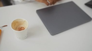 Klinikte çalışan genç adam beyaz önlük ve gözlük takıyor. Yanında kahve ve laptop kullanıyor.