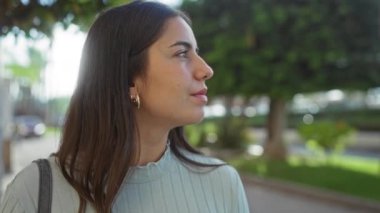 Güneşli bir caddede arka planda ağaçlarla güvenle duran bir kadın sakin ve doğal bir ortam sergiliyor..