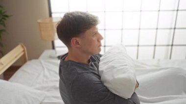 Genç adam dinlenme odasında bir yatakta dinlenirken yastığa sarılıyor.
