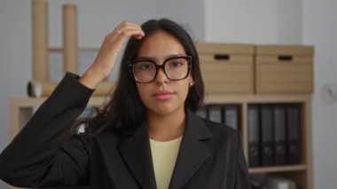 Gözlüklü genç bir kadın işyerinde gülümsüyor. Siyah bir ceket giyiyor.