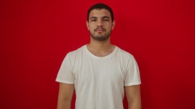 Beyaz tişörtlü İspanyol genç adam mutlu bir galibiyeti kutluyor zafer gülüşü, izole edilmiş kırmızı arka plan üzerinden gülümseme, neşeli bir zaferle eller havaya.