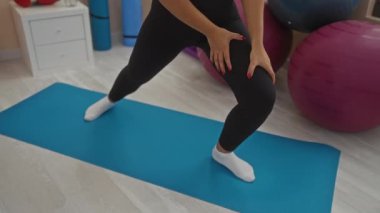 Spor salonundaki mavi bir paspasın üzerinde spor yapan bir kadın spor yaparken bacaklarını ve çoraplarını gösteriyor..