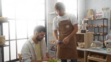 Fırında bir garsonla oturan bir müşteriye yardım eden adamlar kapalı bir kafede ödeme yapmak için telefon kullanıyorlar.