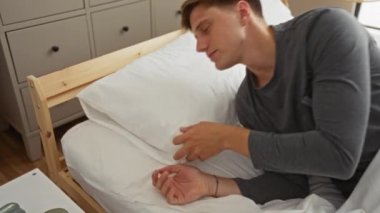 Genç adam rahat bir yatakta beyaz yastıkla rahat bir yatak odasında uyuyor.