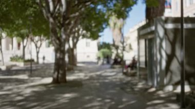 Bulanık manzara, güneşli bir Marsilya caddesinde gölgeler bırakan yapraklı ağaçlar ve Avrupa şehir atmosferini geliştiren yumuşak bokeh görüntülerini yakalıyor..