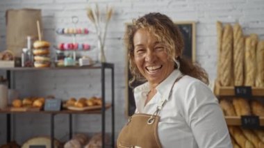 İspanyol kadın gülümsüyor ve arka planda ekmek ve hamur işleri raflarıyla bir pastanede duruyor..