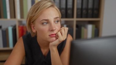 Ofisteki genç kadın kitaplıklar arasında bilgisayarla uğraşırken düşünüyor.