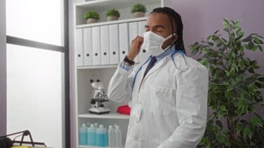 Genç adam klinikte maske çıkarıyor ve gözlerini ovuşturuyor. Hastane işyerinde yorgun görünüyor..