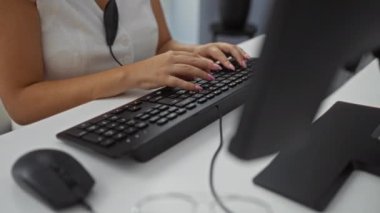 Ofiste çalışan, klavyeye yazı yazan, kulaklık takan, masa başında oturan, arka planda bitki olan, modern bir iş ortamını resmeden bir kadın.