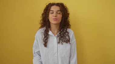 İspanyol asıllı genç bir kadın ayakta dikiliyor ve güzel, seksi bir aşk ifadesiyle öpüşüyor, izole edilmiş sarı arka planda kameraya bakıyor.