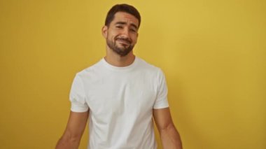 İspanyol adam gülümsüyor ve izole edilmiş sarı bir arka planda büyüleyici bir ifadeye sahip beyaz bir gömlek giyiyor..