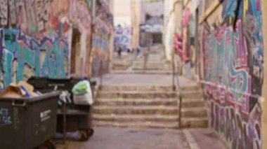Duvarlarında renkli graffitilerle kentsel sokaklar. Bulanık çöp bidonları ve açık hava ortamında merdivenler. Gettonun canlı özünü somutlaştırıyor..