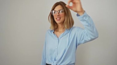 Şok olmuş genç, sarışın bir kadın, gözlük takıyor ve parmaklarının arasından bakıyor. Şaşırmış bir ifadeyle hareket ediyor, beyaz arka planda izole edilmiş.