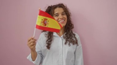 Pembe bir duvarın önünde İspanyol bayrağı tutan kadın gülümsüyor.