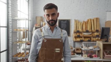 Fırında ekmek ve hamur işi rafları olan genç bir adam, önlük takıyor ve kollarını kavuşturup kapalı bir yerde duruyor, bir iç mekanda kendine güvenen bir portre çiziyor.