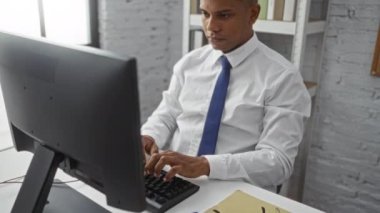 Masaüstü bilgisayarında bir ofiste çalışan genç bir İspanyol profesyonel, modern ve kendini işine adamış bir çalışma ortamını resmediyor.