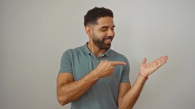 Genç İspanyol adam şaşırmış ve gülümsüyor, elini uzatıyor ve izole edilmiş beyaz arkaplanı işaret ediyor - büyüleyici sunum ve reklam konsepti