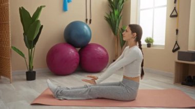 Spor salonunda yoga minderinde denge topları ve bitkilerle egzersiz yapan bir kadın.