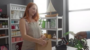 Dekor dükkanında çalışan bir kadın tezgahta para bozdururken bir müşteriye kese kağıdı veriyor.