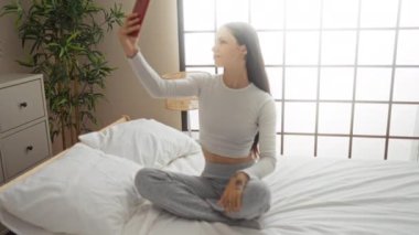 Genç bir kadın modern yatak odasında selfie çekiyor.