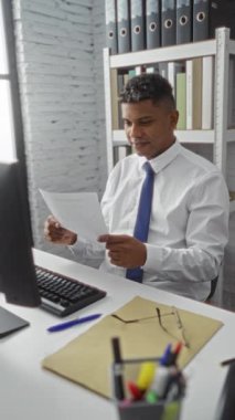 Ofisteki İspanyol adam bilgisayarla doküman okuyor, memnuniyetini ifade ediyor. Etrafı kağıt ve raflarla dolu..