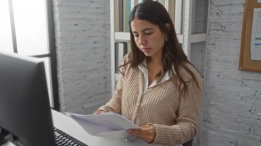 Modern ofiste profesyonel çalışma ortamını gösteren masa başında bilgisayarla doküman okuyan bir kadın.