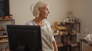 Fırında gülümseyen kadın fırıncı. Raflarda çeşitli ekmek ve hamur işleri sergileniyor.