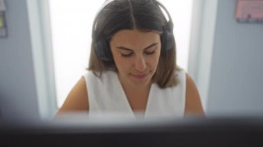 Ofis masasında kulaklık takan bir kadın çalışırken gülümsüyor ve profesyonel ve özenli bir tavır sergiliyor..