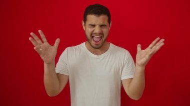 Kazanan! Beyaz tişört giyen genç İspanyol adam başarı için heyecanlanıyor, çılgın zaferi kutluyor, kolları izole edilmiş kırmızı arka planda.