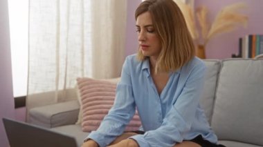 Evde çalışan bir kadın dizüstü bilgisayar sarışın, beyaz, çekici, mavi tişörtlü modern iç mekanı rahatlatıyor..