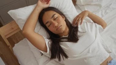 Yatakta uyuyan bir kadın, rahat bir yatak odasında dinlenen esmer bir kadın, rahat bir ev ortamında beyaz yastığın üzerinde dinleniyor.