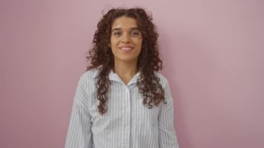 Genç bir kadın kendini göstererek ve alkışlayarak kutlarken izole edilmiş pembe bir arka plana karşı duruyor.