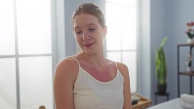 Salondaki bir kadın kendini sakin bir ifadeyle kucaklıyor, açık mavi duvarları ve bitkileri olan parlak bir kapalı kaplıca odasına yerleşiyor.