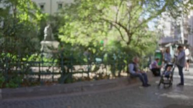 Roma 'nın eski kasabasındaki parke taşı caddesinde güneşli gökyüzü altında yeşil ve bokeh efektli bulanık havanın tadını çıkaran insanlar..