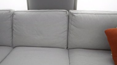 Gri bir koltukta oturan kadın rahat bir oturma odasında telefon kullanıyor modern dekorlu ve doğal ışıklandırmalı, sakin ve rahat bir ev ortamını sergiliyor..