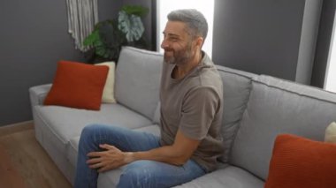 Genç bir adam, rahat bir oturma odasında, koltuğunda oturup arkasını tutarak modern bir dekor ve rahat bir atmosferle rahatsızlığı ya da acıyı öneriyor..