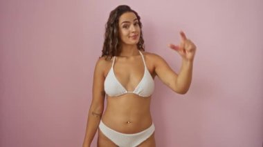 İzole edilmiş pembe arka planda renkli bikinili kadın parmakları, genci, ispanyolcası, el hareketi, boyut ve kendine güveni olan küçük bir beden gösteriyor.