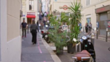 Bulanık yayalar Marsilya, Fransa 'da canlı bir cadde boyunca yürüyorlar. Canlı yeşillikler ve scooterlar kentsel manzarayı canlandırıyor..