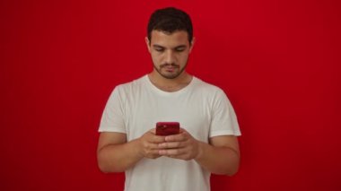 Şaşırdım, genç İspanyol adamın ağzı açık, akıllı telefonda şaşkın, güvensizlik izole kırmızı arka planda, yakalanan korkmuş tepki