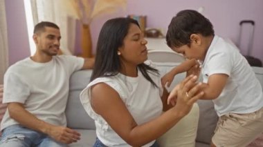 Bir erkek mutlu bir şekilde izlerken, aile sıcak bir oturma odasında çocukla oynayan bir kadınla eğleniyor.