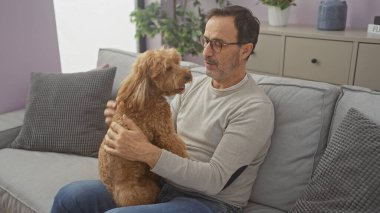 Orta yaşlı İspanyol bir adam evdeki evcil kanişiyle eğleniyor, iç mekan sahnesini canlandırıyor.