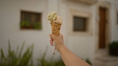 Locorotondo, Puglia 'nın büyüleyici sokaklarında beyaz binalara karşı dondurma külahı tutan kadın İtalya' nın eski kasabasının cazibesini yakalıyor..