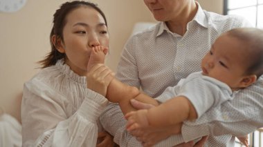 Anne, bebeğin ayağını sevgiyle öperken baba da onu sıcak bir aile ortamında kucağına alır..